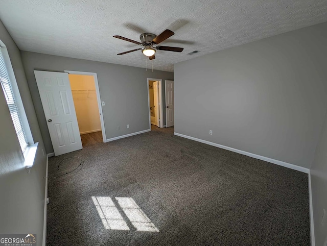 unfurnished bedroom with a spacious closet, dark carpet, ceiling fan, a closet, and a textured ceiling