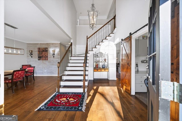 entrance foyer featuring a towering ceiling, a barn door, dark hardwood / wood-style floors, and a notable chandelier