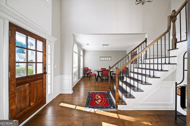 entrance foyer with dark wood-type flooring, a chandelier, and ornamental molding