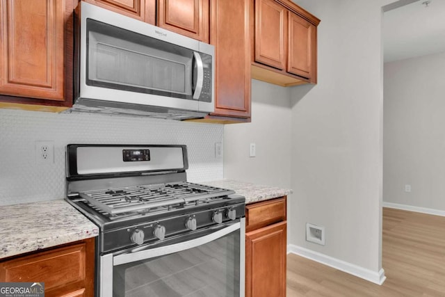 kitchen with decorative backsplash, light stone countertops, stainless steel appliances, and light hardwood / wood-style flooring