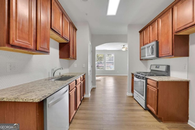 kitchen with light stone countertops, appliances with stainless steel finishes, ceiling fan, sink, and light hardwood / wood-style floors