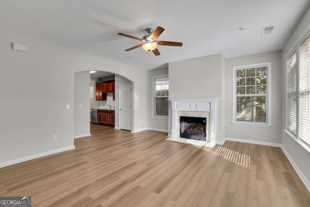 unfurnished living room featuring sink, light hardwood / wood-style flooring, ceiling fan, and a premium fireplace