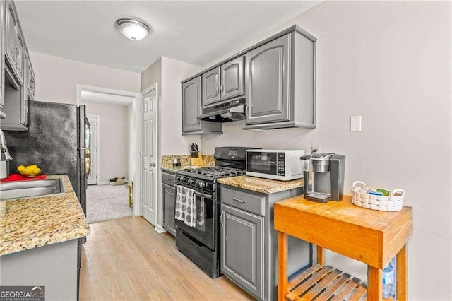 kitchen with light stone counters, light hardwood / wood-style floors, gas stove, sink, and gray cabinets