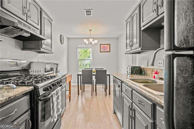 kitchen featuring light stone counters, gray cabinetry, stainless steel appliances, sink, and a chandelier