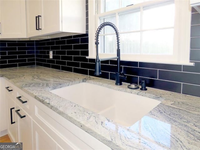 room details with light stone countertops, backsplash, white cabinetry, and sink