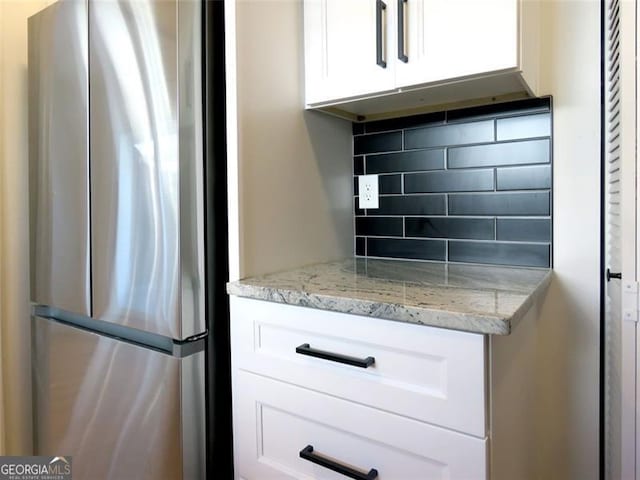 kitchen with white cabinets, stainless steel fridge, backsplash, and light stone countertops