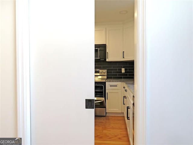 kitchen featuring stainless steel range, light wood-type flooring, tasteful backsplash, and white cabinetry