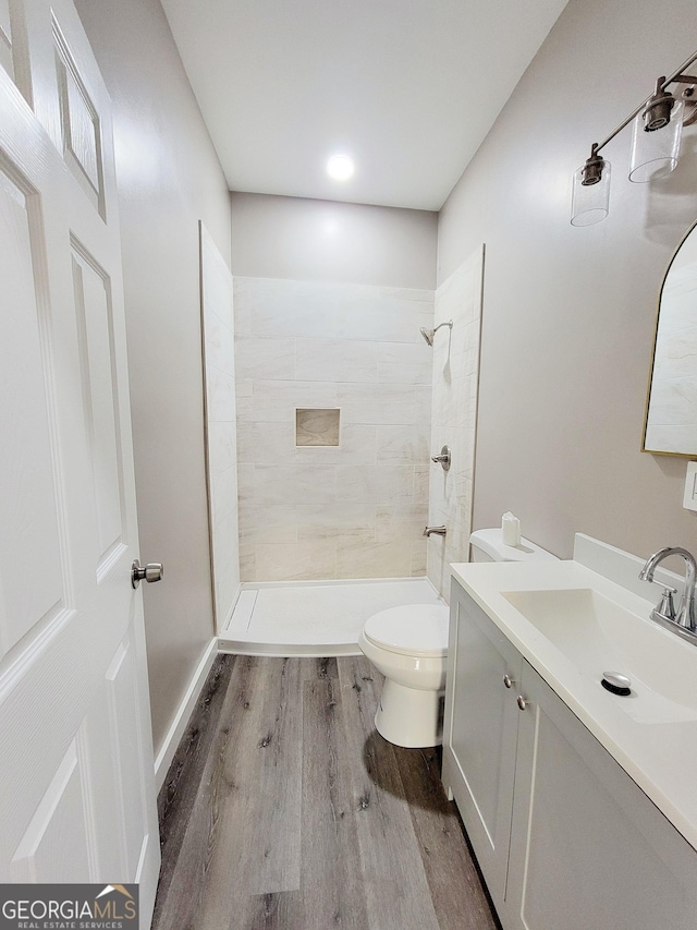 bathroom with tiled shower, vanity, hardwood / wood-style flooring, and toilet