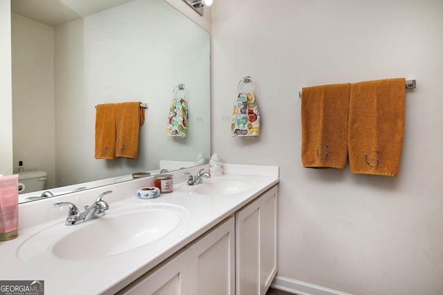bathroom with double vanity, toilet, baseboards, and a sink