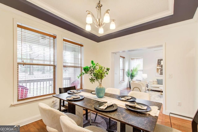 dining space featuring a notable chandelier, a raised ceiling, wood-type flooring, and crown molding