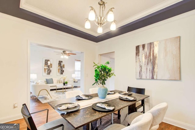 dining room featuring ceiling fan with notable chandelier, hardwood / wood-style flooring, a raised ceiling, and crown molding