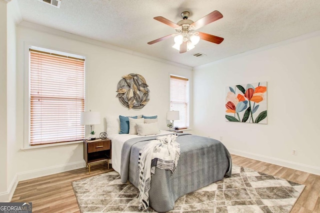 bedroom with hardwood / wood-style floors, ceiling fan, ornamental molding, and a textured ceiling