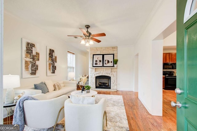 living room featuring ceiling fan, light wood-type flooring, and a fireplace