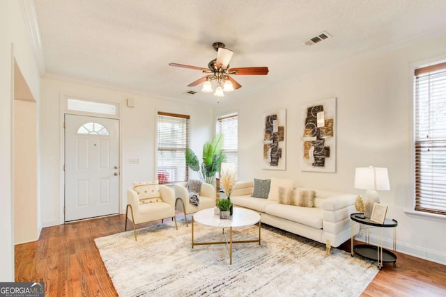 living room with a textured ceiling, hardwood / wood-style flooring, ceiling fan, and crown molding