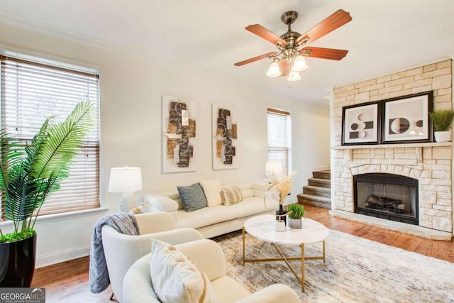 living room featuring ceiling fan, a stone fireplace, and wood-type flooring