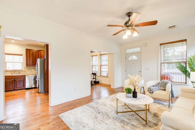 living room featuring ceiling fan, light hardwood / wood-style floors, sink, and crown molding