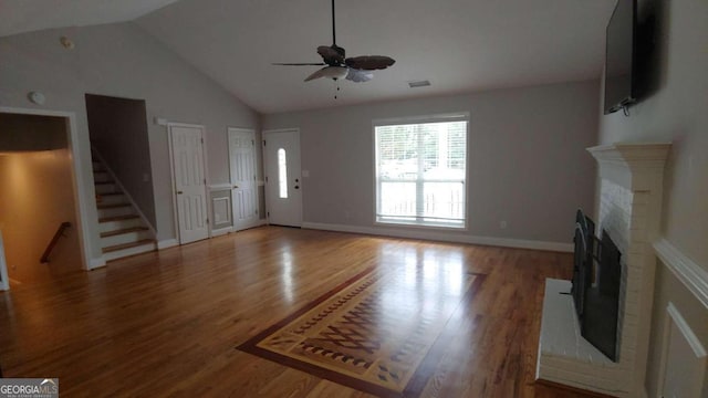 unfurnished living room featuring ceiling fan, hardwood / wood-style floors, vaulted ceiling, and a brick fireplace