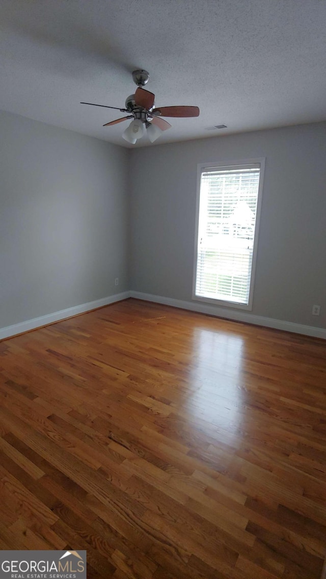 unfurnished room with a textured ceiling, ceiling fan, and dark wood-type flooring