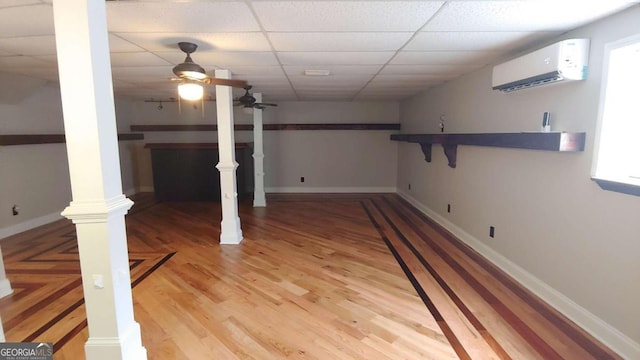 basement with a wall mounted air conditioner, a drop ceiling, hardwood / wood-style flooring, and ceiling fan