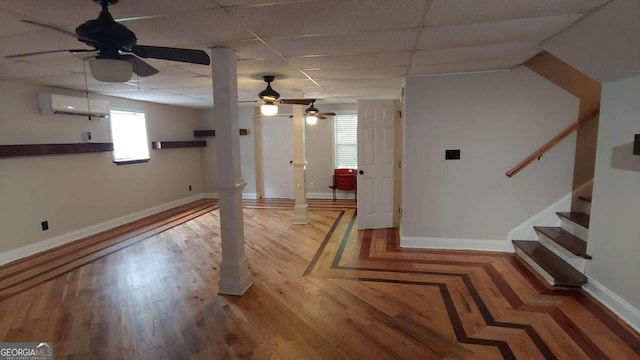 basement with a paneled ceiling, ceiling fan, hardwood / wood-style floors, and a wall unit AC