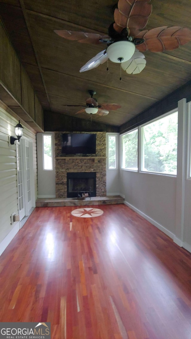 unfurnished living room featuring hardwood / wood-style floors, wood walls, a stone fireplace, and wood ceiling