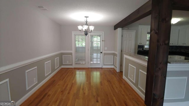 unfurnished dining area with hardwood / wood-style floors, beam ceiling, and an inviting chandelier