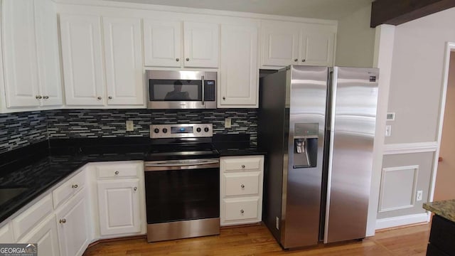 kitchen featuring white cabinets, stainless steel appliances, dark stone counters, and light hardwood / wood-style floors