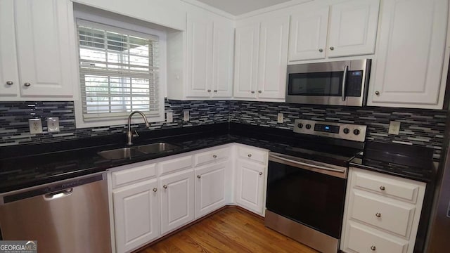 kitchen featuring appliances with stainless steel finishes, tasteful backsplash, sink, dark stone countertops, and white cabinetry