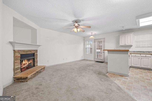 unfurnished living room with light carpet, a fireplace, ceiling fan, and a textured ceiling