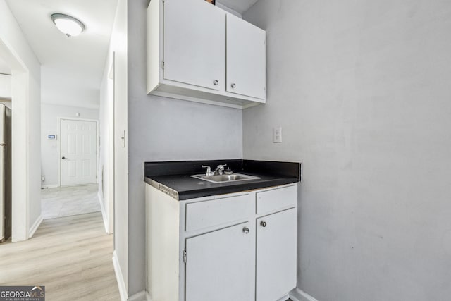 kitchen featuring white cabinets, stainless steel fridge, light wood-type flooring, and sink