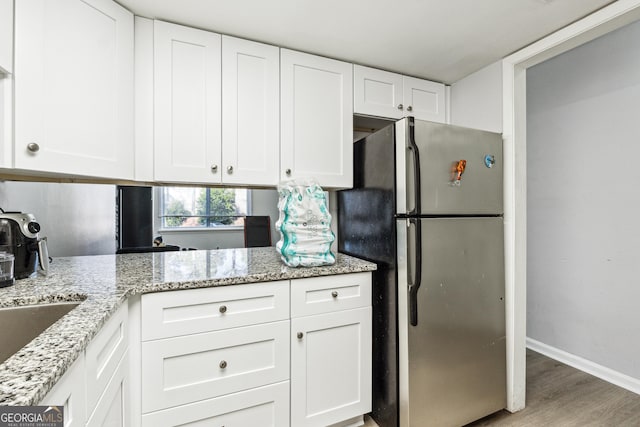 kitchen with stainless steel fridge, white cabinets, light stone countertops, and light wood-type flooring