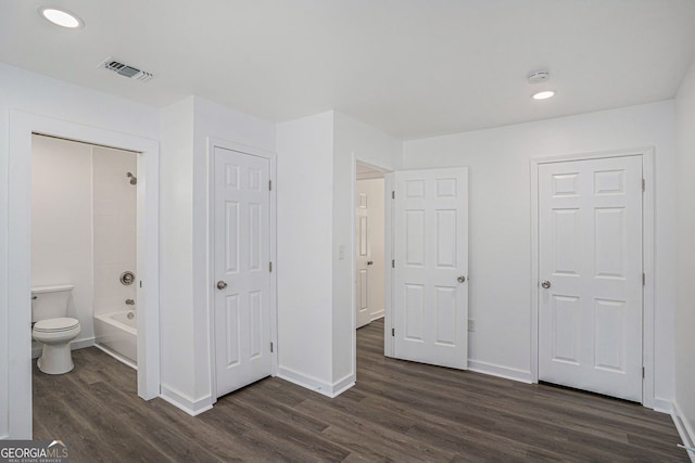 unfurnished bedroom featuring ensuite bathroom and dark hardwood / wood-style flooring