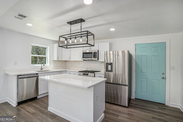 kitchen with sink, white cabinetry, hanging light fixtures, appliances with stainless steel finishes, and a kitchen island