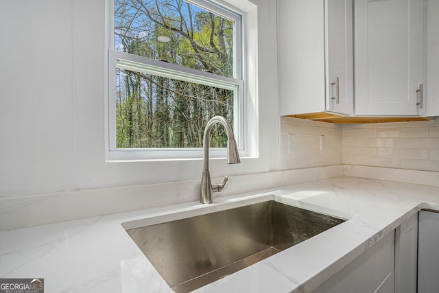 interior details featuring sink, decorative backsplash, light stone countertops, and white cabinets