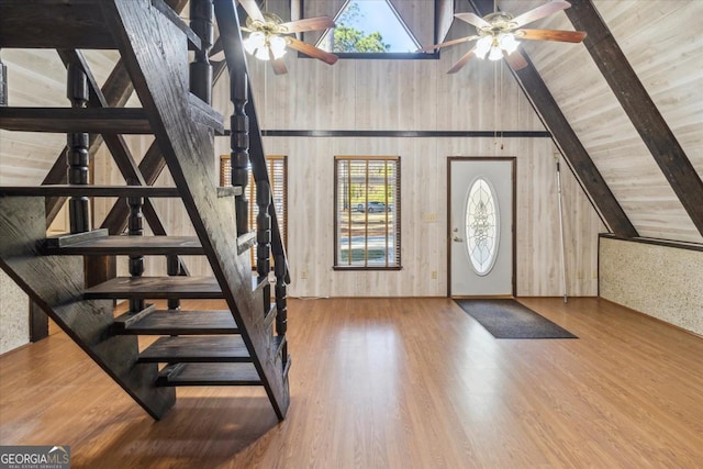 entrance foyer featuring a ceiling fan, stairway, wooden walls, and wood finished floors