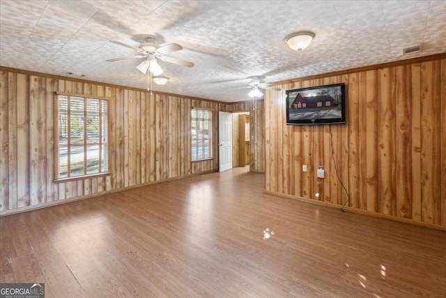 unfurnished living room featuring visible vents, baseboards, a ceiling fan, wood finished floors, and crown molding