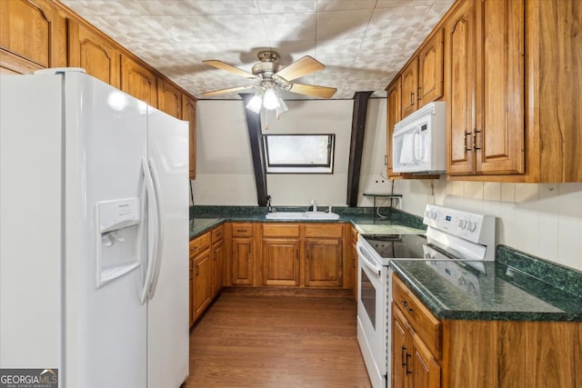 kitchen featuring white appliances, brown cabinetry, a sink, and wood finished floors