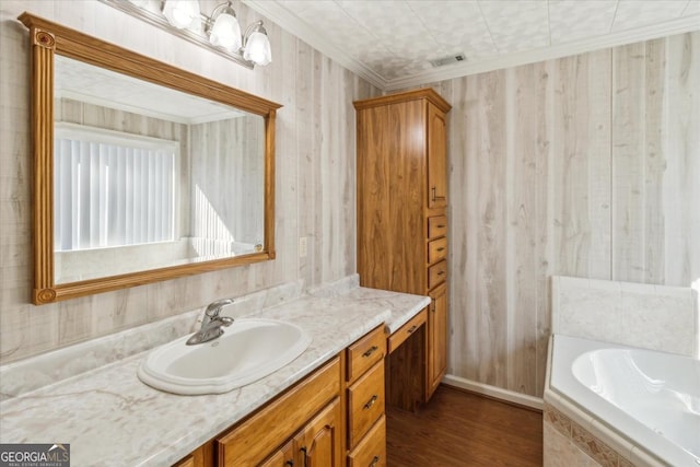 bathroom with tiled bath, wood finished floors, visible vents, vanity, and crown molding