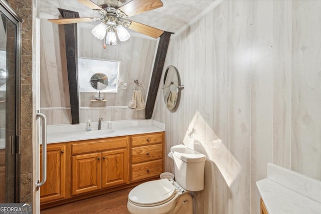 bathroom with toilet, a ceiling fan, a shower with shower door, vanity, and wood finished floors