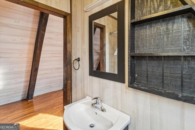 bathroom with wood finished floors, wood walls, and a sink