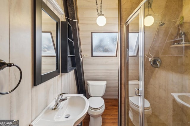 bathroom with toilet, a sink, wooden walls, a shower stall, and wood finished floors