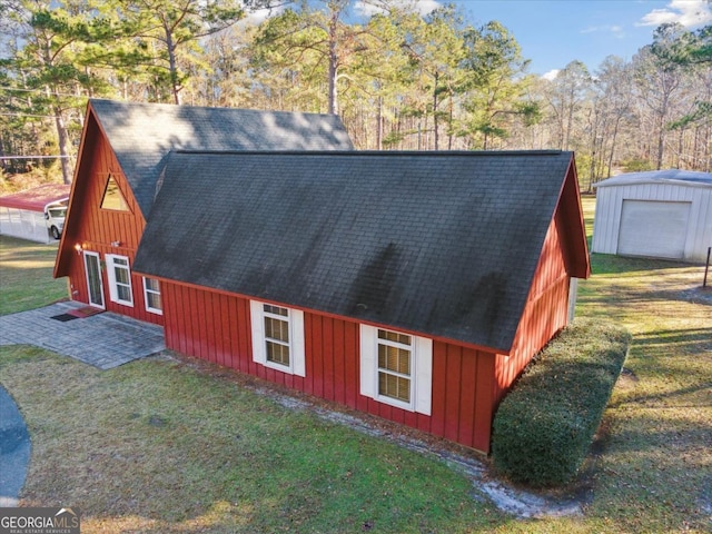 view of property exterior featuring a patio, roof with shingles, an outbuilding, a yard, and board and batten siding