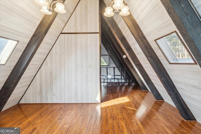 additional living space with lofted ceiling with skylight, wood-type flooring, and an inviting chandelier