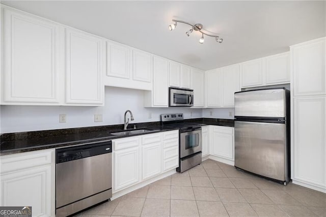 kitchen featuring dark stone counters, stainless steel appliances, sink, light tile patterned floors, and white cabinetry