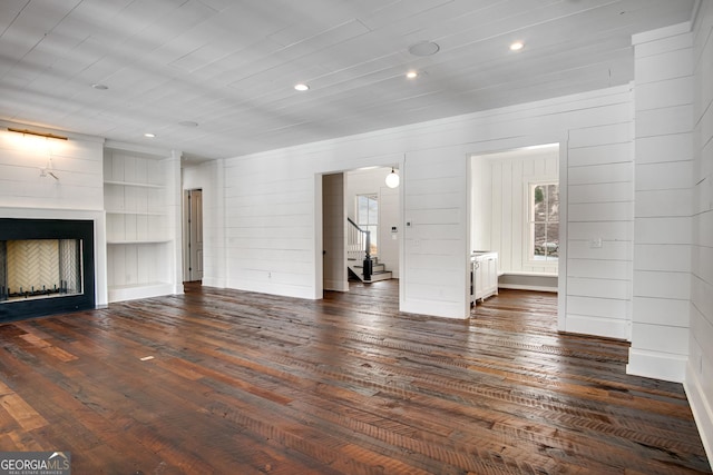 unfurnished living room with built in shelves, dark wood-type flooring, and wood walls