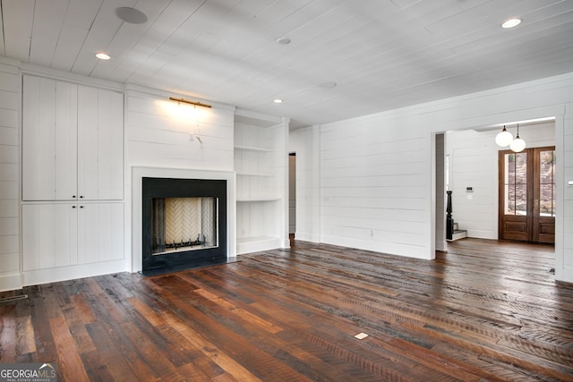 unfurnished living room with french doors, dark hardwood / wood-style flooring, built in features, and wood walls