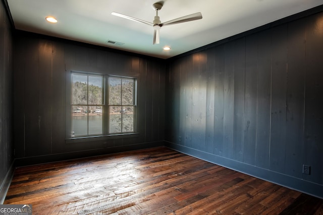 unfurnished room with ceiling fan, wood walls, and dark wood-type flooring