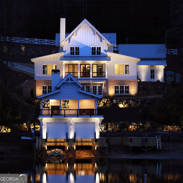 back house at night featuring a balcony and a water view