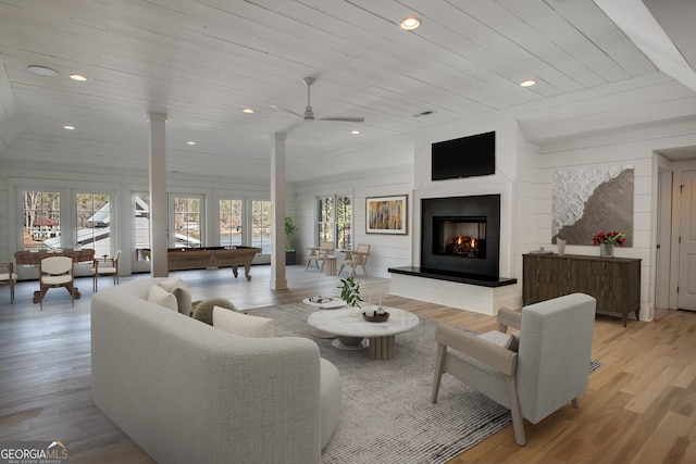 living room featuring wooden walls, light hardwood / wood-style flooring, ceiling fan, wood ceiling, and decorative columns