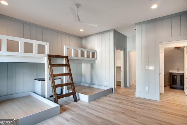 bedroom featuring wood walls, ensuite bathroom, ceiling fan, and light hardwood / wood-style flooring